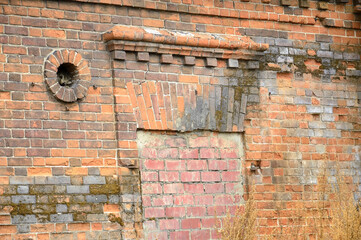 Fragment of an old red brick wall. Bricked window opening with decoration and lined round opening. The wall is overgrown with moss