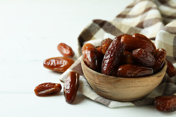 Bowl of dried dates on kitchen napkin on white wooden background