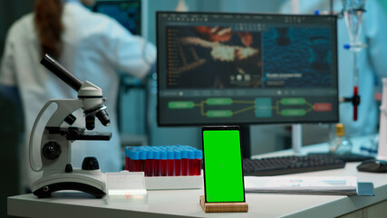 Display phone with green screen, mock up on template placed on desk in scientific lab while team of medical researcher scientists analysing virus evolution at digital monitor conducting experiment