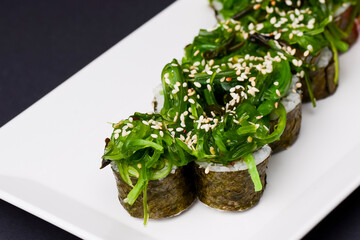 Japanese sushi with rice and fish and seaweed salad on top. Served on a white plate over black background.
