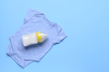 Bottle of milk for baby and clothes on color background