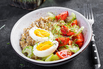 Breakfast oatmeal porridge with boiled egg, cherry tomatoes, celery and microgreens. Healthy balanced food.