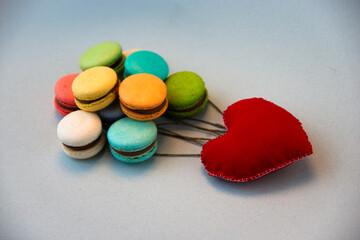 Multicolored macarons like balls and a red heart on a gray background.