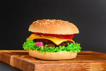 Bacon and beef patty burger with red onions and cheese over black background. Fast food, junk food concept.