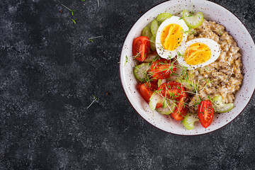 Breakfast oatmeal porridge with boiled egg, cherry tomatoes, celery and microgreens. Healthy balanced food. Top view, above, copy space