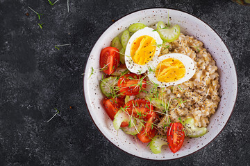 Breakfast oatmeal porridge with boiled egg, cherry tomatoes, celery and microgreens. Healthy balanced food. Top view, above, copy space