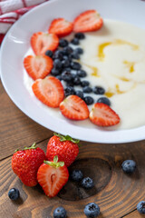Semolina porridge with strawberries and blueberries in a white plate on the brown wooden table