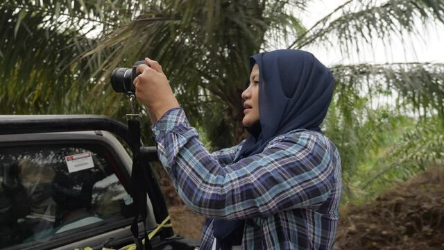 Asian female muslim photographer or videographer holding camera and shooting natural wildlife from open car, safari trip in the wild, nature journey traveling tourist