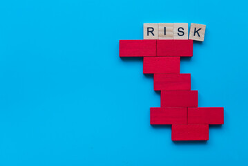Risk concept with alphabet of risk on unstable structure of red wooden domino on blue background.