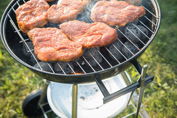 Marinierte Schweine Fleisch Nackensteaks roh grillen mit Rauch auf Holzkohle Kugelgrill im Garten an Sommer Abend