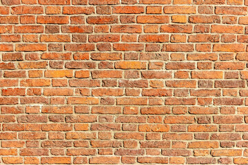 A wall of old, cracked bricks, with a weathered and faded surface. Restored brickwork of an old house.