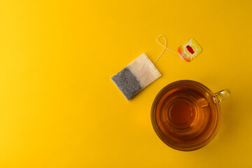 Teabag and cup of tea on yellow background.