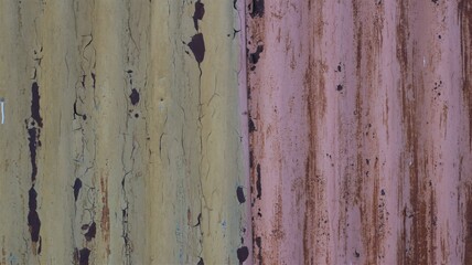 rusty iron fence made of corrugated bent metal painted in pinkish and brownish colors with the texture of old scratched cracked paint, a fragment of an aged worn shabby surface