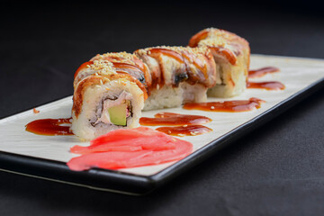 Sushi set, sushi rolls with cream cheese and eel served on a white plate over black background.
