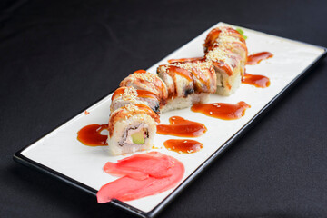Sushi set, sushi rolls with cream cheese and eel served on a white plate over black background.