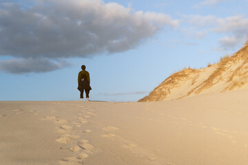 Fototapeta na wymiar Persona joven caminado por arena blanca con dunas en playa y dejando las huellas de los pies en la arena, con un bonito cielo azul con nube.
