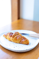 Top view Croissants and cutlery housed in a white plate on a wooden table in a cafe shop.