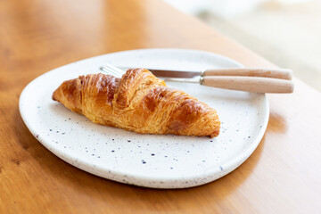 Top view Croissants and cutlery housed in a white plate on a wooden table in a cafe shop.