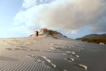 Fototapeta na wymiar Mujer joven con los brazos extendidos en la cumbre de una duna de arena blanca con una poca vegetación