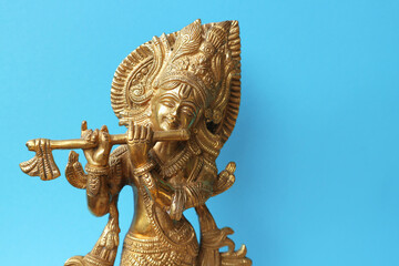 Lord Krishna is a golden sculpture on a blue background with space for text.
