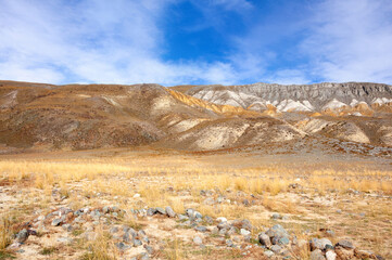 Scenic view over Akkol valley, surrounded by colorful hills and mountains, stone formations, harsh environment on a sunny day with blue sky and clouds. Altai autumn landscape, Russia