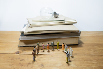 group of miniature business people meeting on wooden table and pile of books with light bulb.