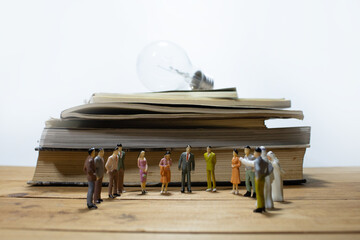 group of miniature business people meeting on wooden table and pile of books with light bulb.
