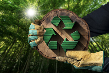 Hands with protective work gloves holding a recycling symbol made of green and brown wood inside of...