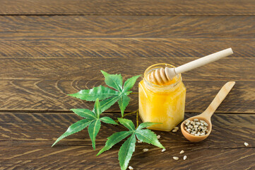 Cannabis honey in a bowl with wooden deeper, hemp leawes amd seeds on wooden table