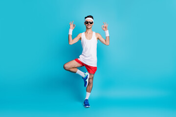 Full size photo of sporty guy doing crossfit train show okay sign wear wristband gumshoes isolated blue color background