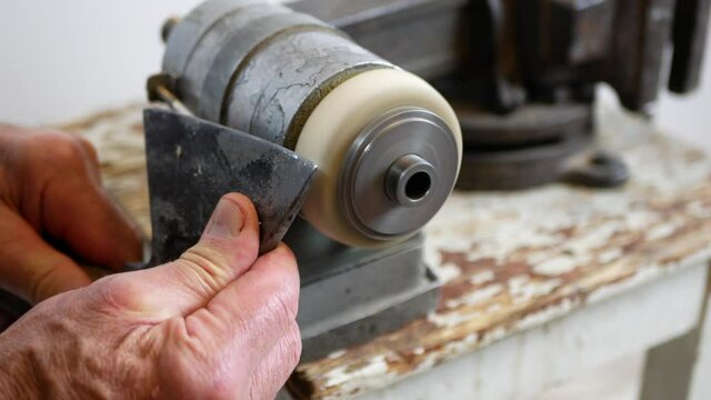 Man is sharpening the axe blade using grinding machine, sparks are flying