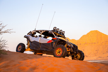 Modern dune buggy parked on sand in the desert with mountains in the background, Fossil Rock, Sharjah, United Arab Emirates, side view. © Cleop6atra