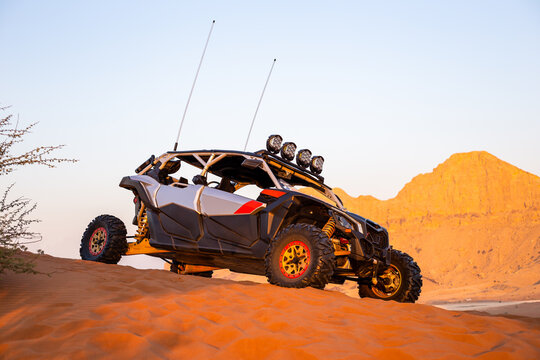 Modern dune buggy parked on sand in the desert with mountains in the background, Fossil Rock, Sharjah, United Arab Emirates, side view.