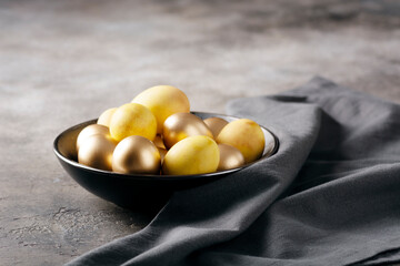 Easter table setting, golden Easter eggs in a deep plate on a dark concrete background, selective focus, horizontal orientation