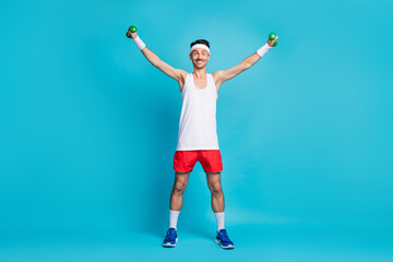 Full length photo of young sportsman happy positive smile do physical exercises with small barbells isolated over blue color background