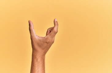 Arm and hand of caucasian man over yellow isolated background picking and taking invisible thing, holding object with fingers showing space