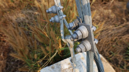 Bolt fixed on guy wire. U-BOLT or clamp with bolt attached to the metal anchor on the concrete base to support the tension of electric pole with copy area. Selective focus