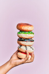 Hand of hispanic man holding tower of donuts over isolated pink background.