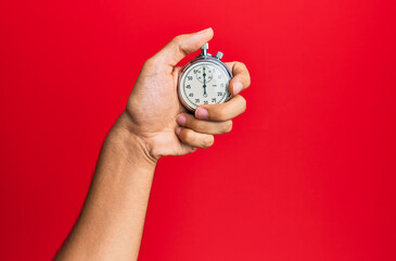 Hand of young hispanic man using stopwatch over isolated red background.