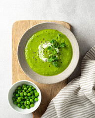 Green pea soup in a ceramic bowl on gray concrete background, top view