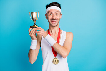 Fototapeta Photo of young cheerful sportive man happy positive smile win competition hold trophy isolated over blue color background obraz