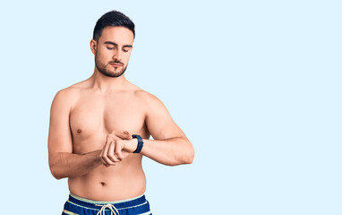 Young handsome man wearing swimwear checking the time on wrist watch, relaxed and confident
