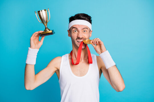 Photo of brown haired lucky man win medal golden trophy bite teeth isolated on blue color background