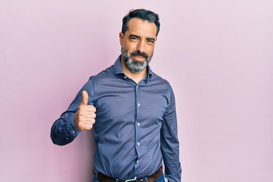 Middle age man with beard and grey hair wearing business clothes doing happy thumbs up gesture with hand. approving expression looking at the camera showing success.