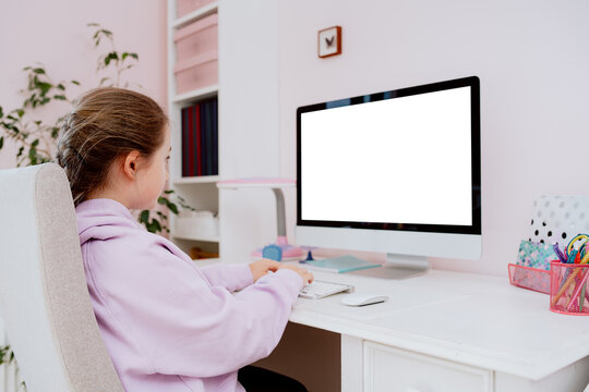 A view from behind the back of a teenage school girl who uses a desktop computer while sitting at a desk in her room. She participates in remote learning and checks content posted on social media.