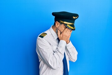 Middle age man with beard and grey hair wearing airplane pilot uniform with sad expression covering...