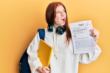 Young red head girl wearing student backpack holding passed test angry and mad screaming frustrated and furious, shouting with anger. rage and aggressive concept.