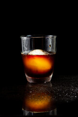 Cold americano decoration with ice ball in whisky glass on a black table.