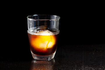 Cold americano decoration with ice ball in whisky glass on a black table.