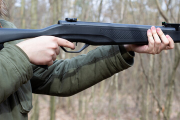 Young man shoot with air pneumatic rifle, spring daytime, hands holding gun